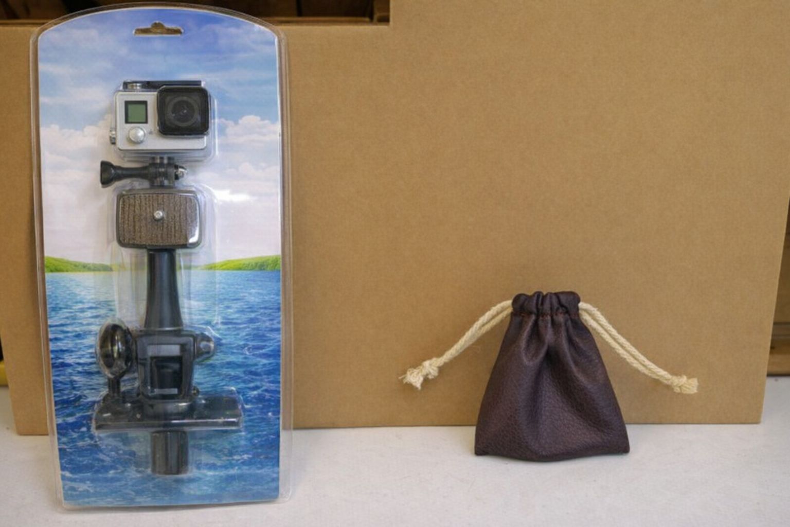 GoPro Action-Kamera in Originalverpackung neben einem kleinen braunen Lederbeutel.